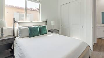A neatly arranged bedroom with a bed, bedside tables, a nightstand, and a door.