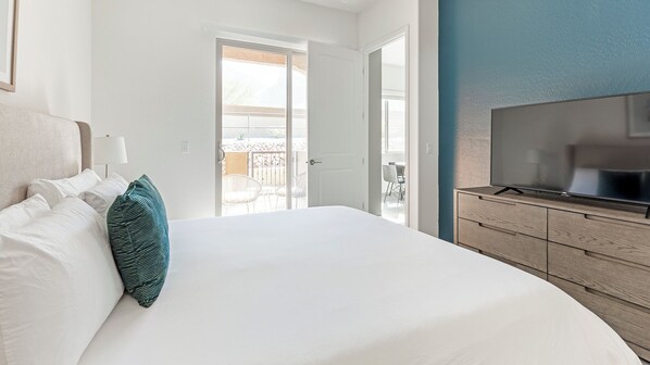 A hotel room with a large bed, a television on a wooden dresser, and a balcony with outdoor furniture. - Landing Apartments Oro Valley (Oro Valley)