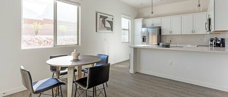 A modern kitchen with white cabinets, a stainless steel refrigerator, and a dining area with a round table and chairs.