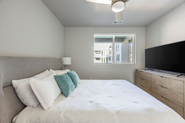 A bedroom with a bed, a TV, a dresser, a window, and a ceiling fan. - Landing at RED (Reno)