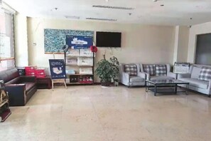 A hotel lobby with a sofa, armchairs, a coffee table, a television, and a plant. - Cinda Hotel (Zhaoyuan)