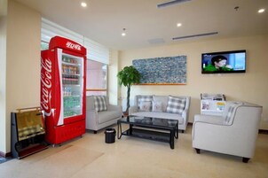 Una sala de estar con un refrigerador rojo Coca-Cola, un televisor montado en la pared y un juego de sofá.