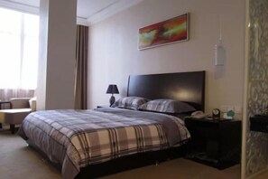 Ein Hotelzimmer mit Bett, Nachttisch, Lampe, Gemälde und Stuhl.