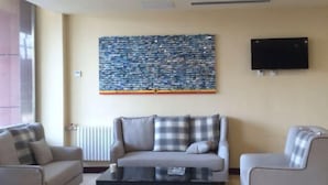 A modern living room with a sofa, armchairs, a coffee table, a large abstract painting, and a flat-screen TV mounted on the wall. - Cinda Hotel (Zhaoyuan)