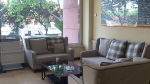 A living room with two sofas, a coffee table, and a large window with a view of trees and a building outside. - Cinda Hotel (Zhaoyuan)