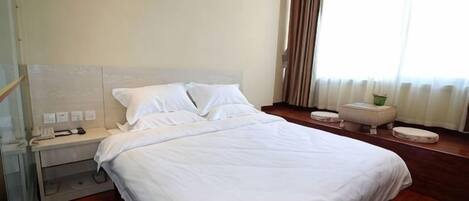 Una habitación de hotel con una cama grande, mesita de noche y una ventana con cortinas.