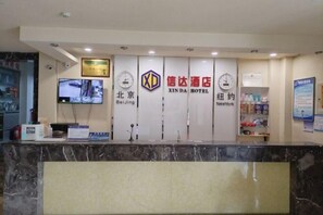 Ein Hotelrezeptionstresen mit einem digitalen Bildschirm, Uhren und einem Schild für das XINDA HOTEL in Peking und New York.
