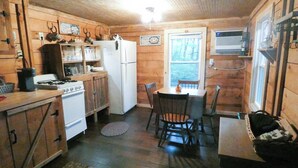 A rustic cabin-style kitchen with wooden walls, a stove, refrigerator, and a dining area with chairs and a table.