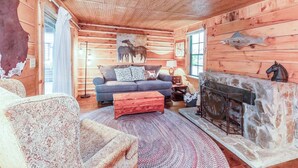 A log cabin interior with a fireplace, a sofa, a patterned armchair, and a rug.