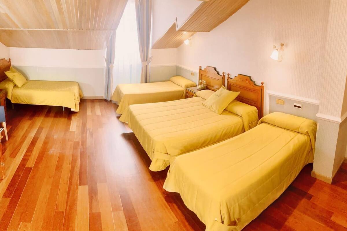 Habitación de hotel con cuatro camas individuales, piso de madera y techo inclinado.