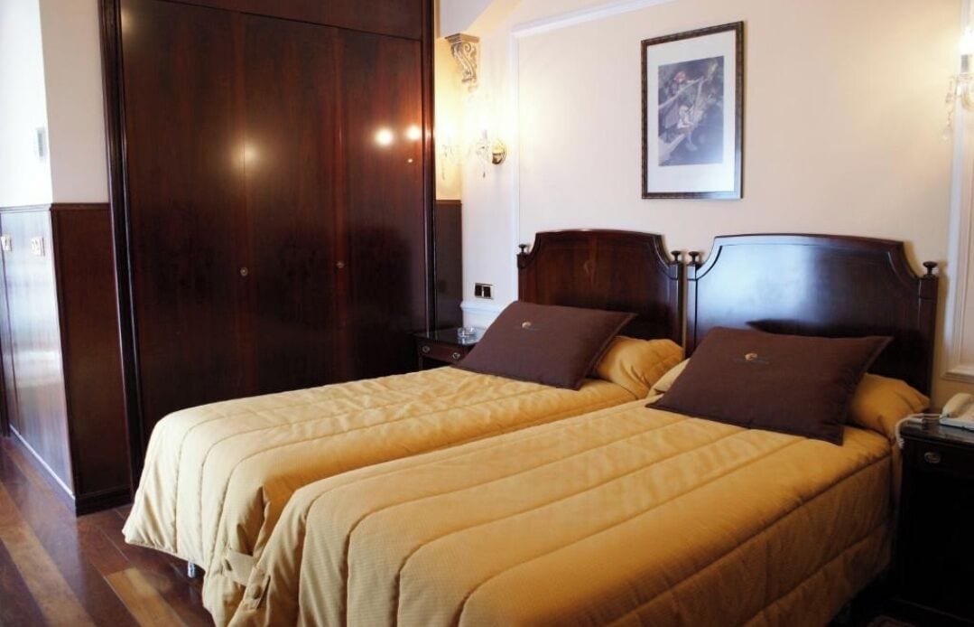 Habitación de hotel con dos camas, cabeceros de madera, una mesita de noche y un cuadro en la pared.