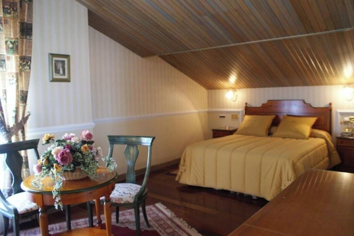 Un dormitorio con techo de madera, una cama con colcha color beige, una mesita de noche y una silla con un arreglo floral.