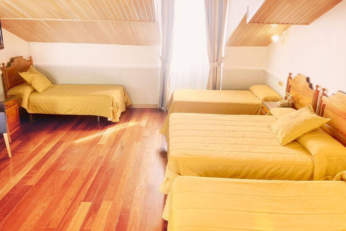 Habitación con tres camas, piso de madera y techo inclinado.
