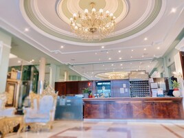 Un lobby de hotel con una gran araña, una recepción y muebles ornamentados.