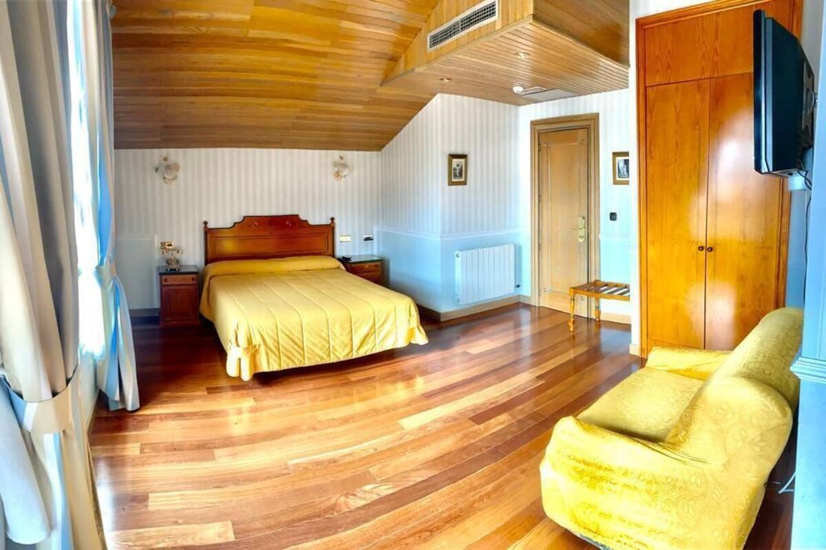 Un dormitorio con piso de madera, una cama con cubrecama amarillo, un armario de madera y un televisor montado en la pared.
