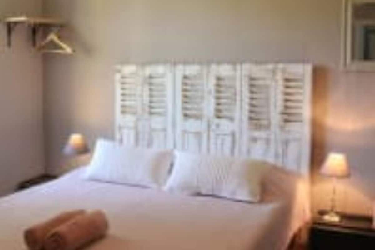 A hotel room with a large bed, a nightstand, and a wall-mounted light fixture.