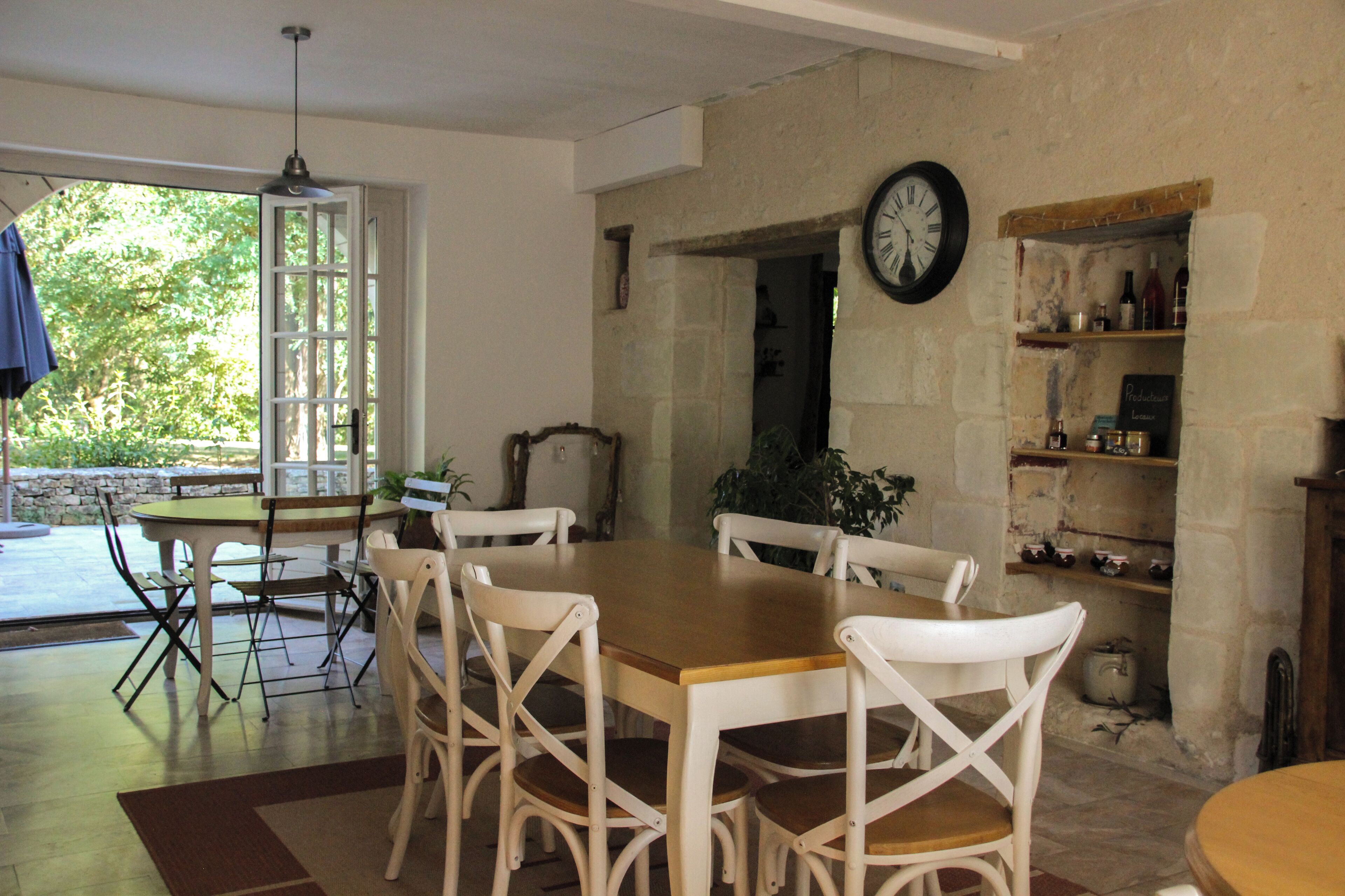 Un comedor con una mesa de madera y sillas blancas, un reloj en la pared y una pared de piedra con estantes.