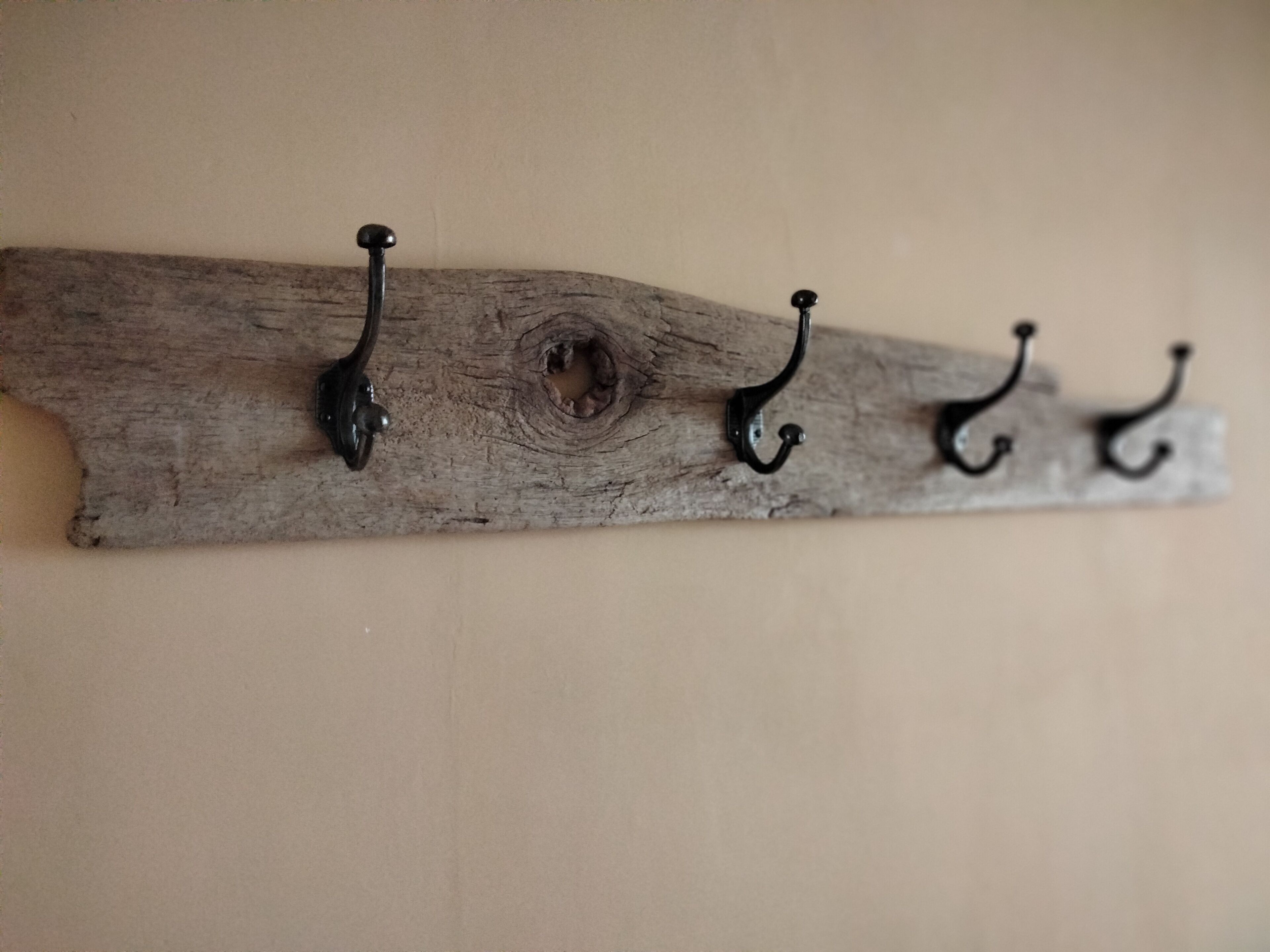 A rustic wooden wall-mounted rack with four metal hooks.