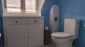 A bathroom with a white toilet, a white cabinet with two doors, a window with a striped curtain, and a blue wall.