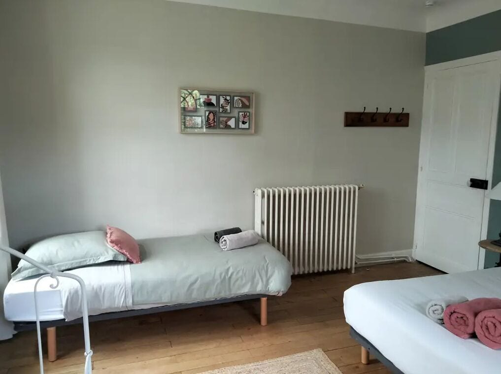 Un dormitorio con dos camas, un radiador, un perchero y una obra de arte en la pared.