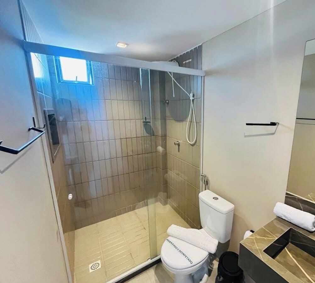 A modern bathroom with a glass-enclosed shower, a toilet, and a sink with a marble countertop.