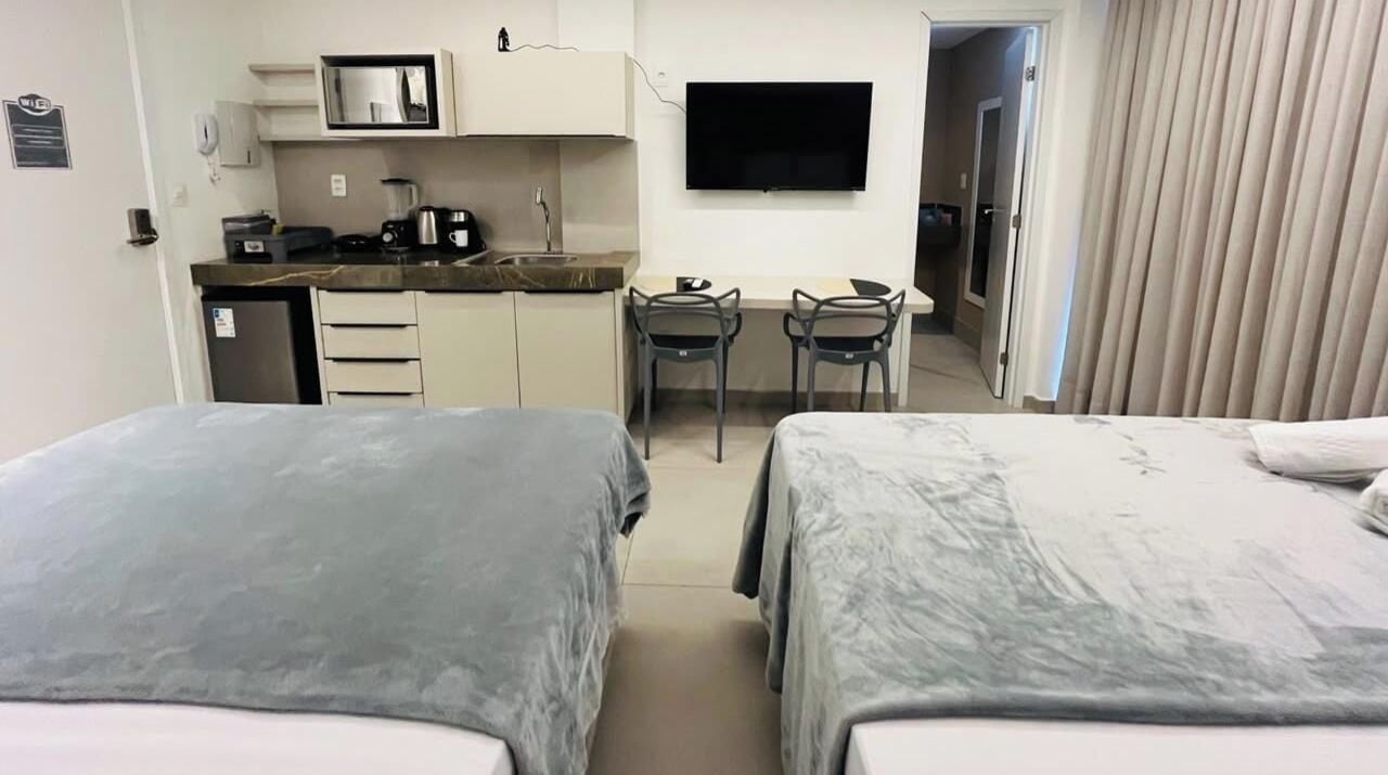 A hotel room with two beds, a kitchenette, a flat-screen TV, and a desk with two chairs.