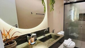 Une salle de bain moderne avec un grand miroir, un lavabo doté d’un plan de toilette en marbre, des toilettes et une cabine de douche en verre.
