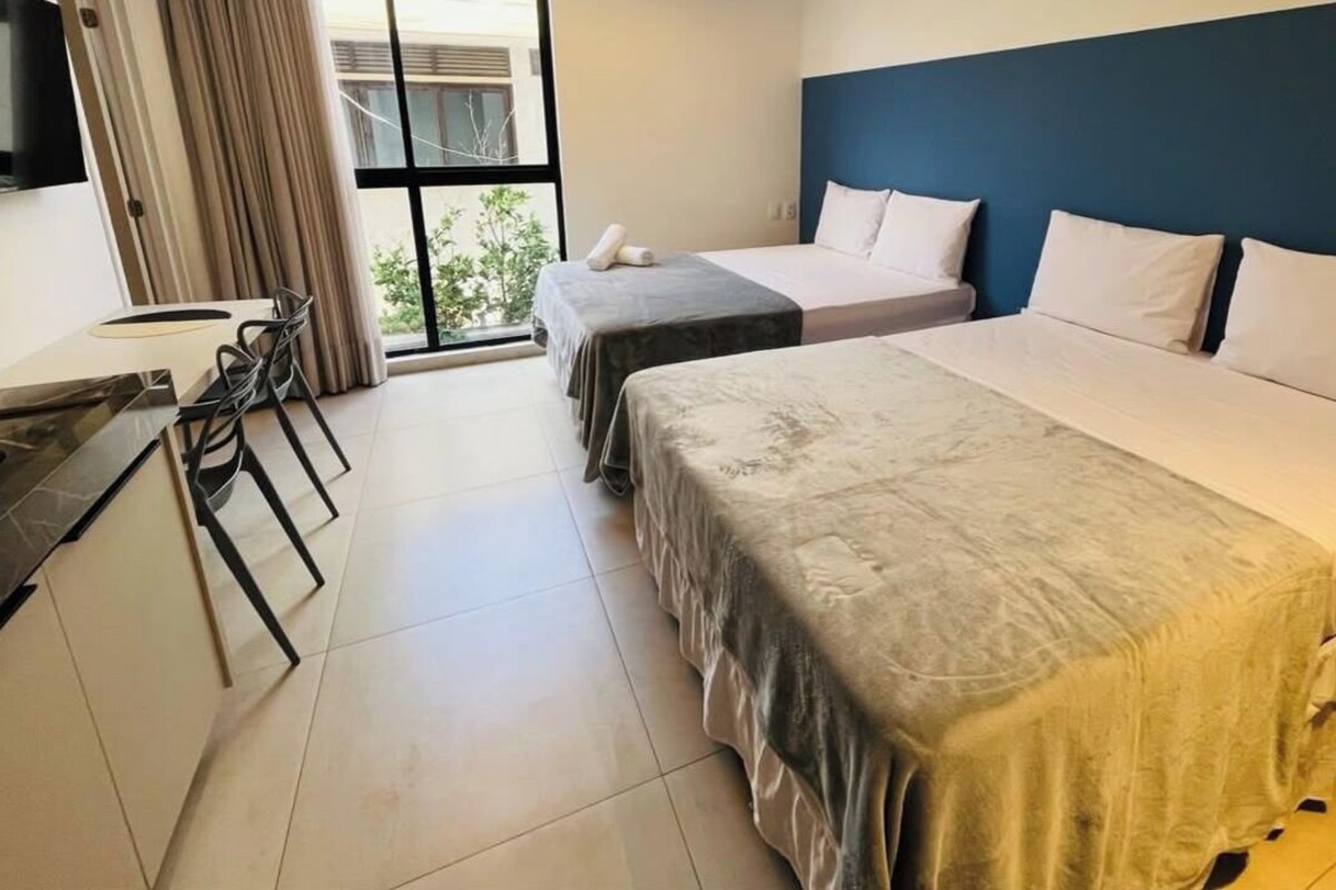 Una habitación de hotel con dos camas, un escritorio y vistas al exterior.