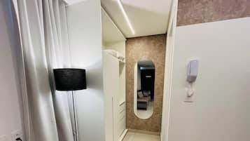 Quarto de hotel com cama, espelho, telefone e porta com interruptor de luz.