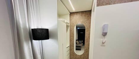 A hotel room with a bed, a mirror, a telephone, and a door with a light switch.