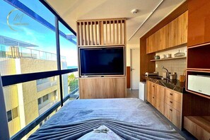 A modern kitchen with a large TV, wooden cabinets, and a view of the city. - LM OZEAN (Joao Pessoa)