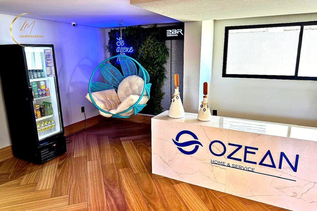 A reception area with a vending machine, a hanging chair, and a reception desk with the logo 'OZEAN HOME & SERVICE'.