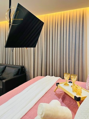 A hotel room with a bed, a TV, a massage table, and a tray with golden cups.