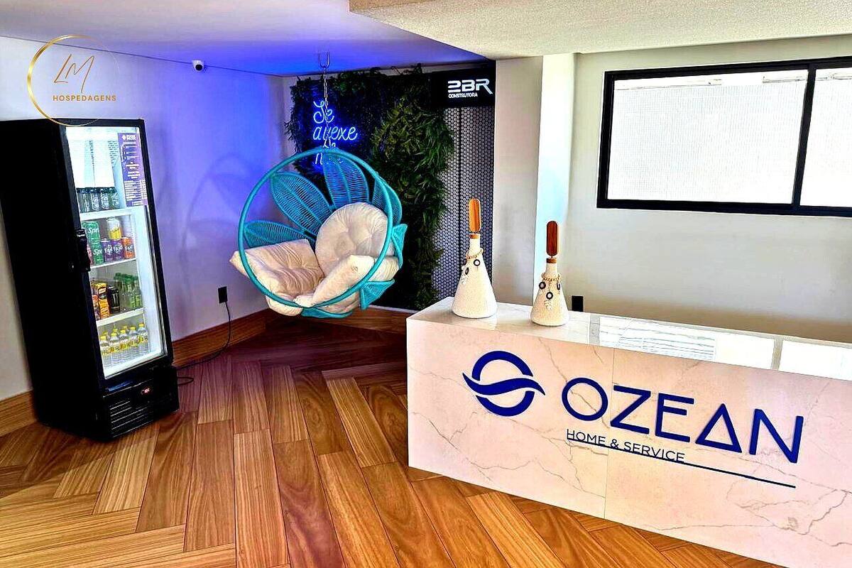 A reception area with a vending machine, a hanging chair, and a reception desk with the logo 'OZEAN HOME & SERVICE'.