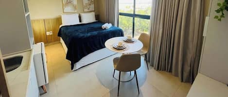 A hotel room with a bed, a round dining table with chairs, a small desk, and a window with curtains.