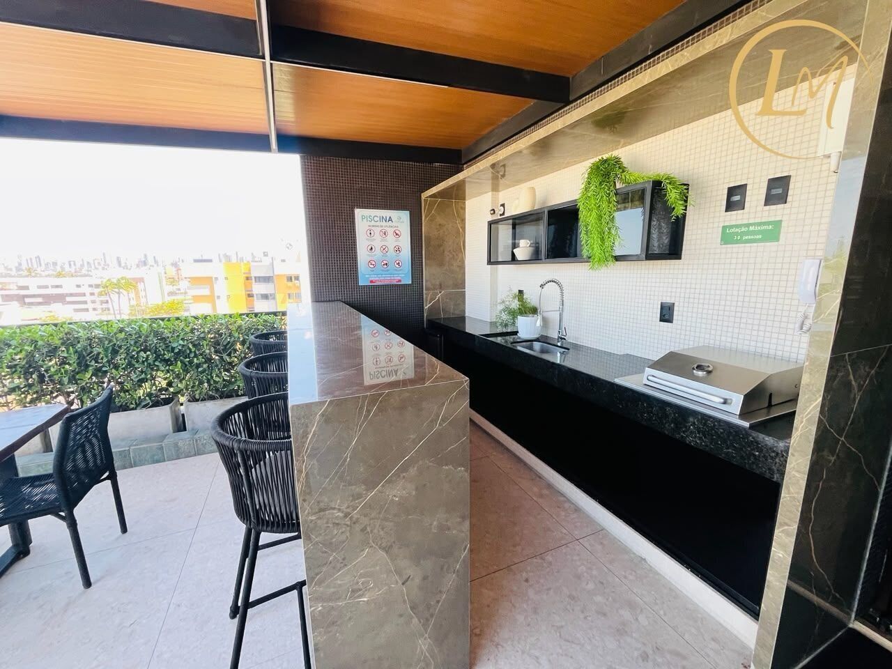 A modern kitchen with a black countertop, a sink, and a window with a view of the city. There are chairs and a table outside the kitchen.