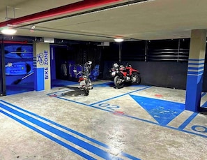A motorcycle parking area with blue lines and numbers, a bike zone sign, and a red motorcycle.