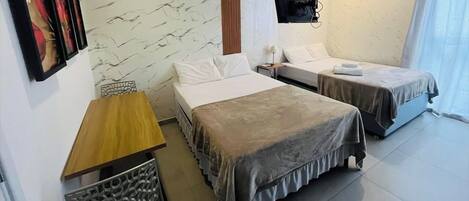 Una camera d'albergo con due letti, un comodino in legno, un pannello decorativo a parete e una TV fissata al muro.