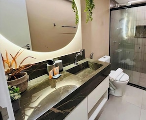 A modern bathroom with a large mirror, a sink with a marble countertop, a toilet, and a glass shower enclosure. - LM OZEAN (Joao Pessoa)