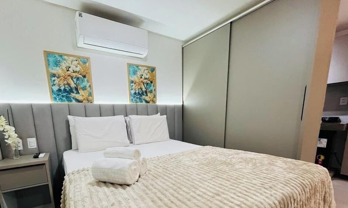 Una habitación de hotel con cama, mesita de noche y aire acondicionado instalado en la pared.