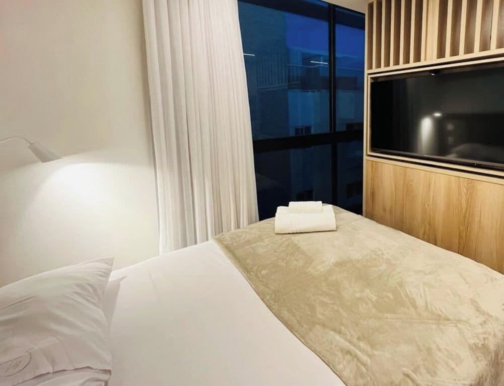 Una habitación de hotel con cama, ventana con cortinas y panel de madera.
