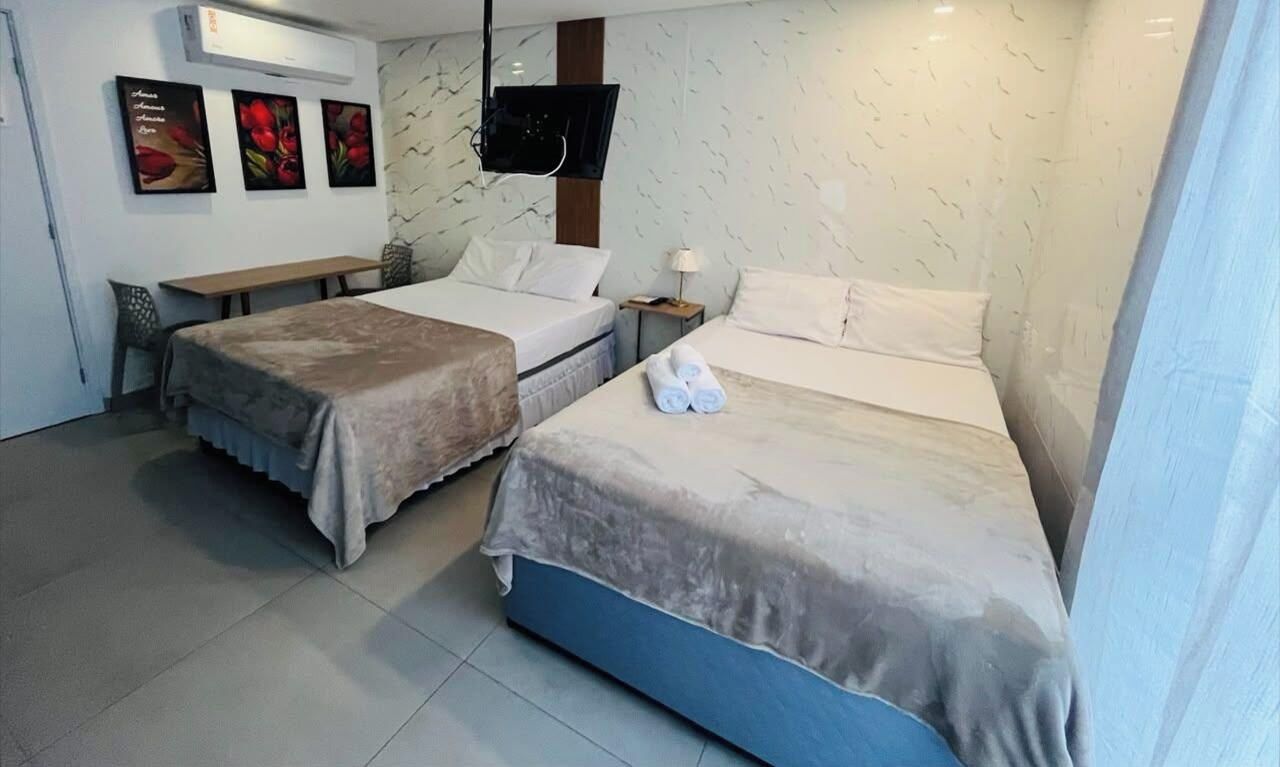 Habitación de hotel con dos camas, un escritorio, una silla, un televisor y decoración en la pared.