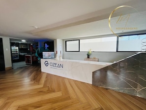 A reception desk with a logo, a counter, a small plant, and a window. - LM OZEAN (Joao Pessoa)