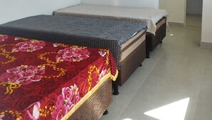 Ein Zimmer mit zwei Betten, eines mit einer blumigen Tagesdecke und das andere mit einer schlichten Hülle. An der Wand ist eine Klimaanlage angebracht.