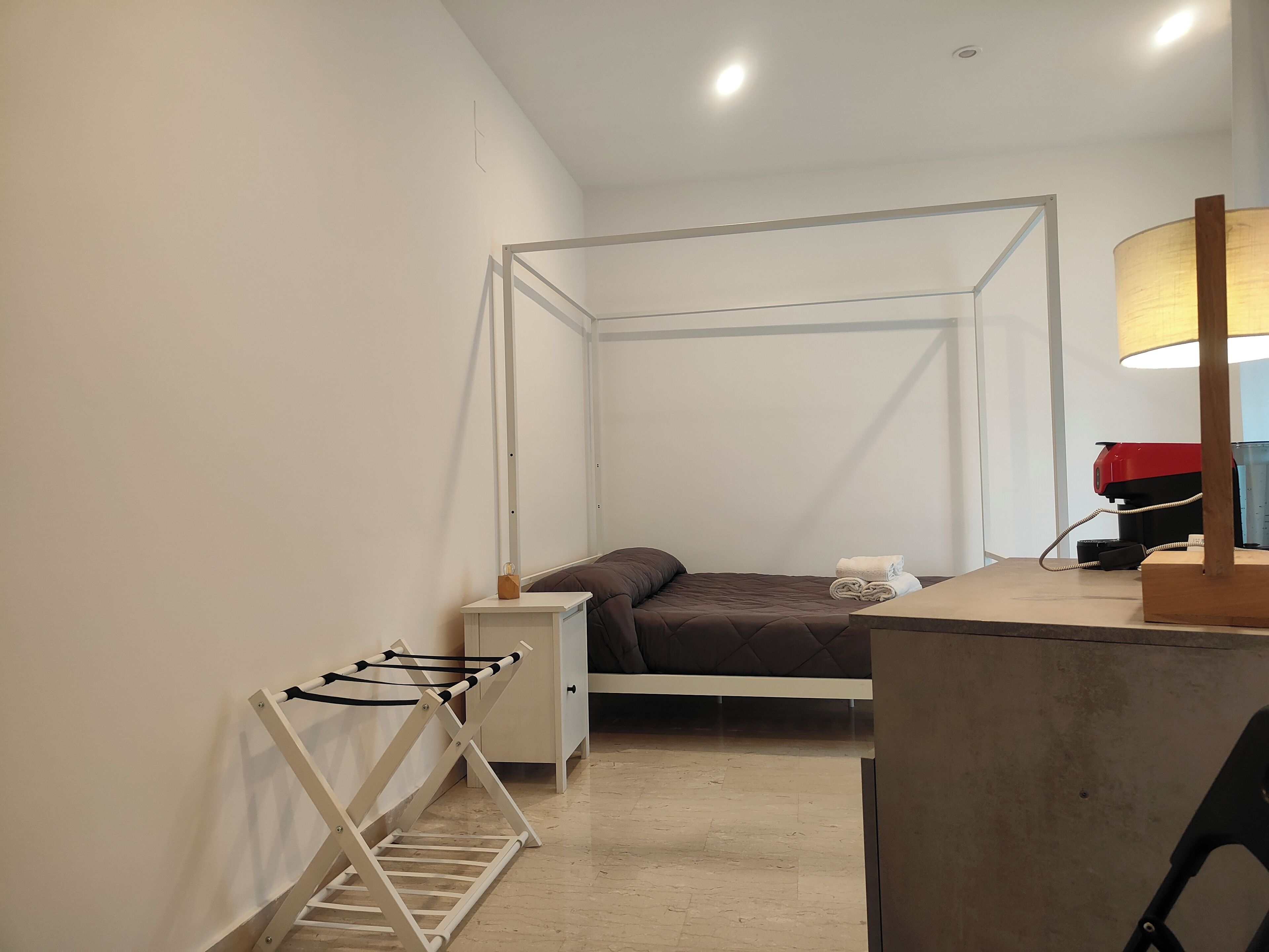 A bedroom with a four-poster bed, a bedside table, a lamp, and a desk with a chair.