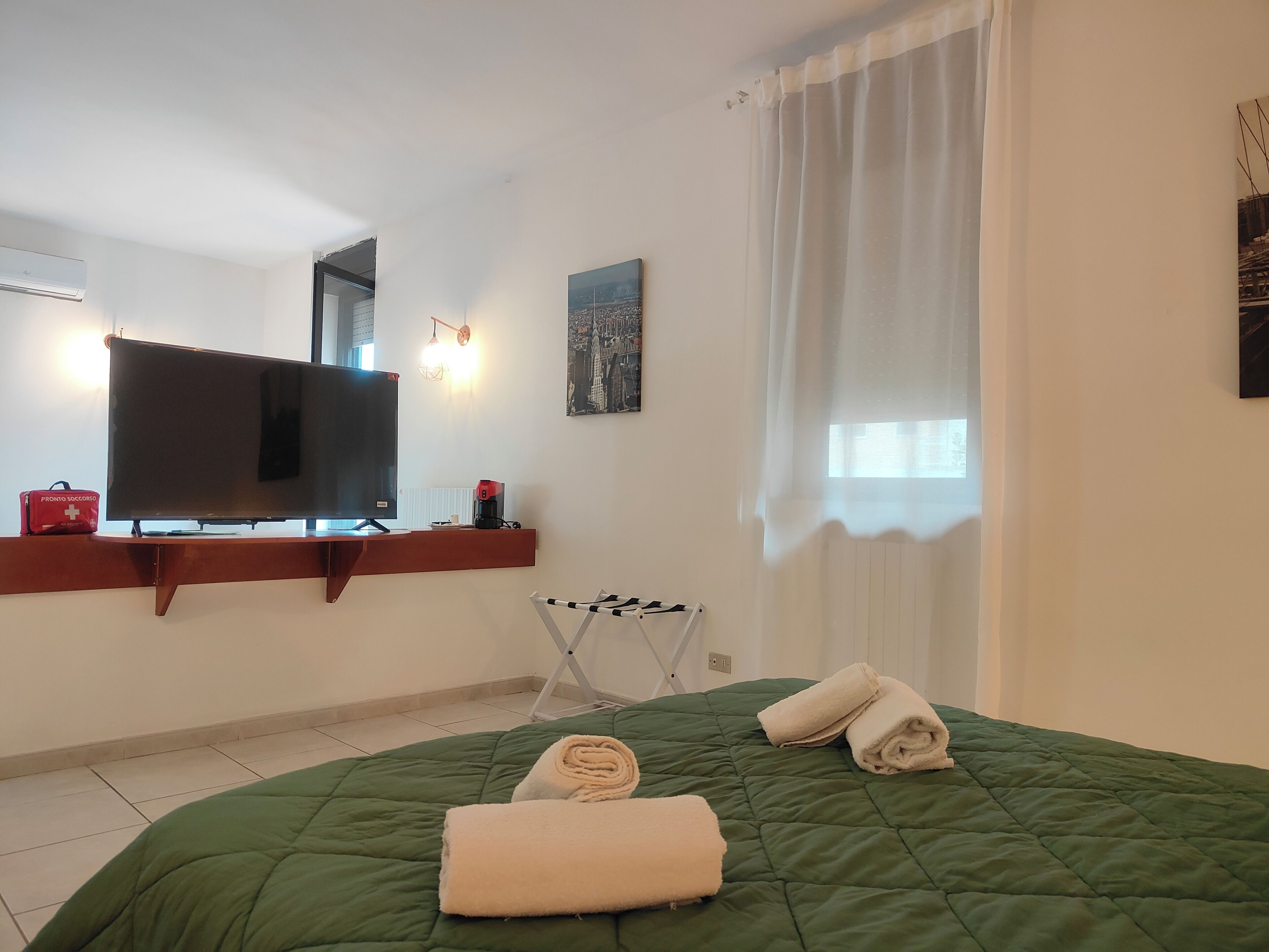 A hotel room with a bed, a television, a red bag, a white towel, and a window with curtains.