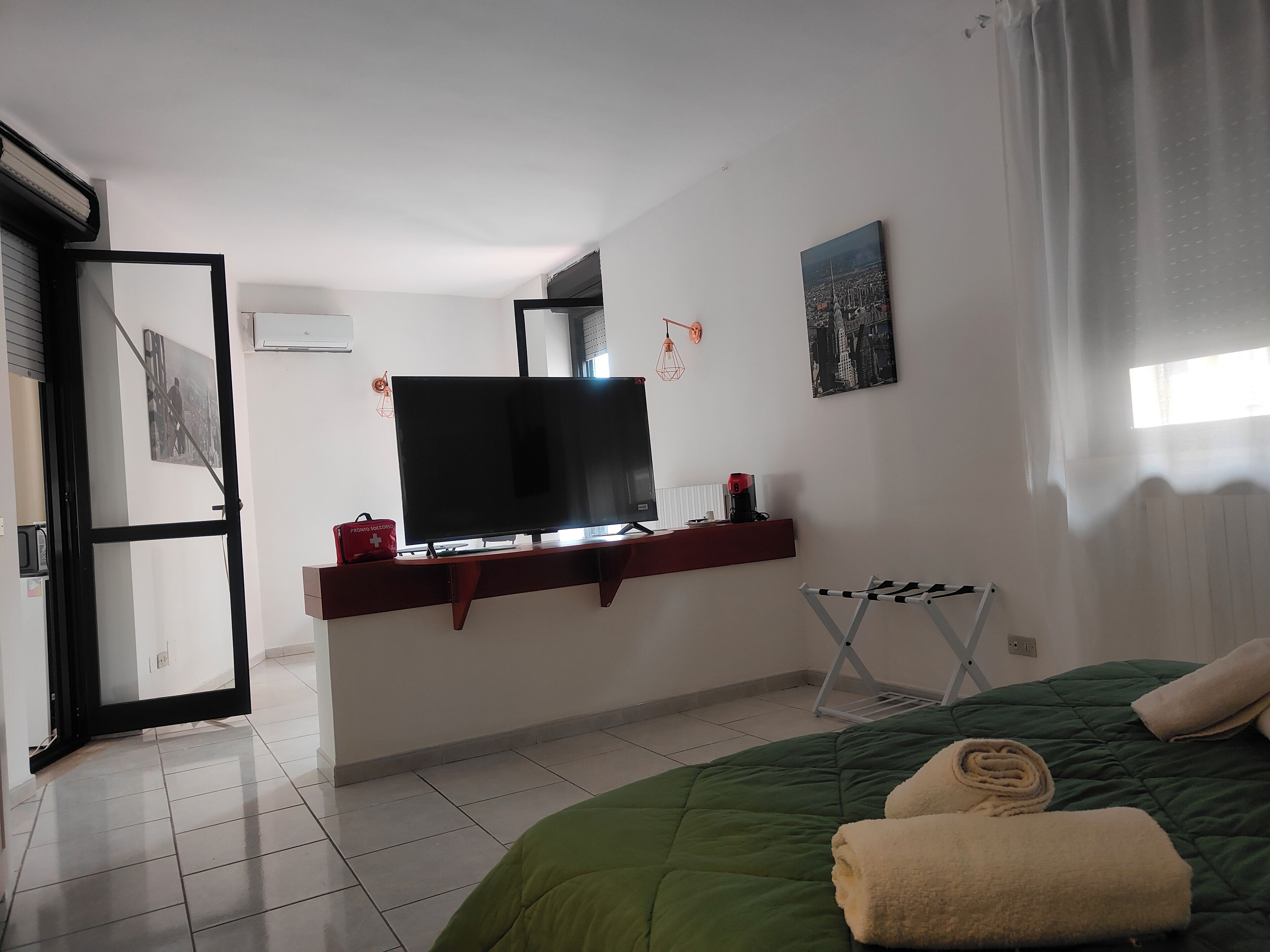 Ett hotellrum med en säng, en tv, en röd väska och ett fönster med gardiner.