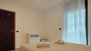A bedroom with a bed, a bedside table, a TV, and a window with curtains. - CconfortHotels eXtramurale Apartment (Bari)
