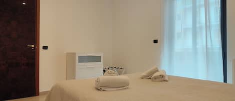 A bedroom with a bed, a bedside table, a TV, and a window with curtains.