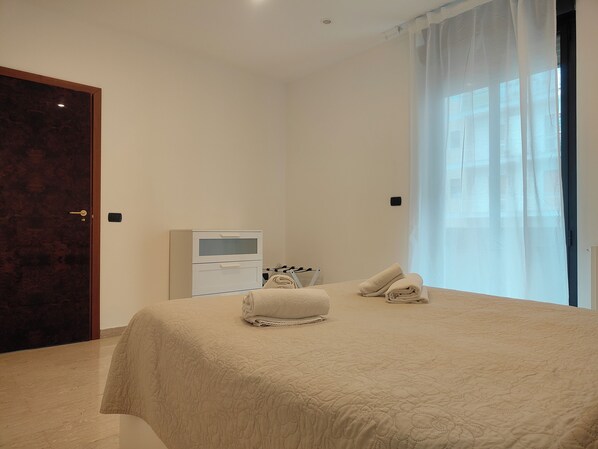 A bedroom with a bed, a bedside table, a TV, and a window with curtains.